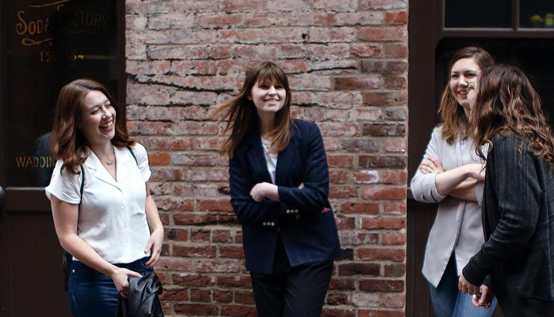 Four woman chatting, smiling and laughing outside near brick wall
